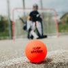 Orange ball with 'Road Warrior' branding on a sports field with a goal and players in the background.